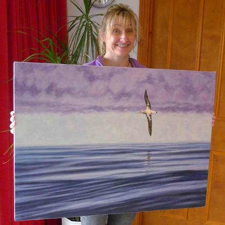 A girl holding a oil painting of a Albatross flying over the sea.